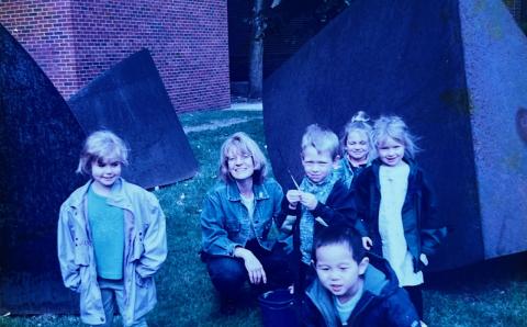 Ann Ruhl Carlson with a group of preschool children in front of a metal sculpture