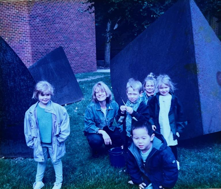 Ann Ruhl Carlson with a group of preschool children in front of a metal sculpture