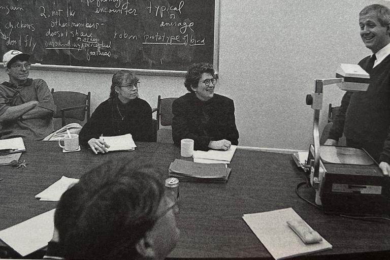 Professor Andrew Collins instructs a class of graduate students seated at a table