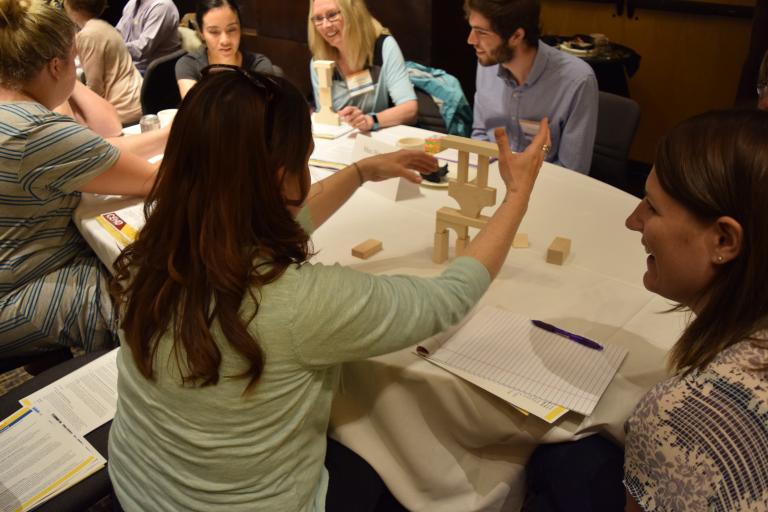 Conference table with adults gathered around doing an activity with play wooden blocks
