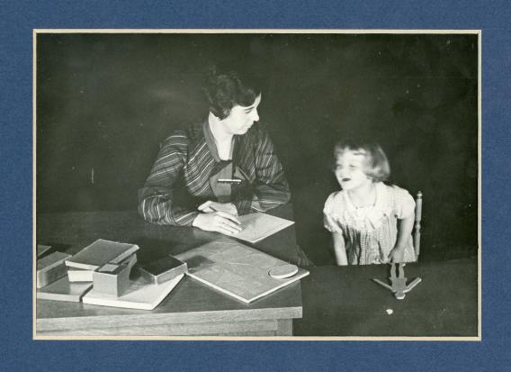 1930s era photo of a female researcher at a table with a toddler