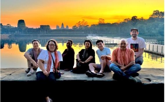 CEHD Cambodia delegation members on a stone ledge in front of a reflective river with a sunrise above them