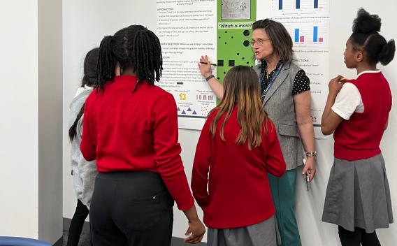 ICD Professor Melissa Koenig stands in front of a research poster with a group of middle school students