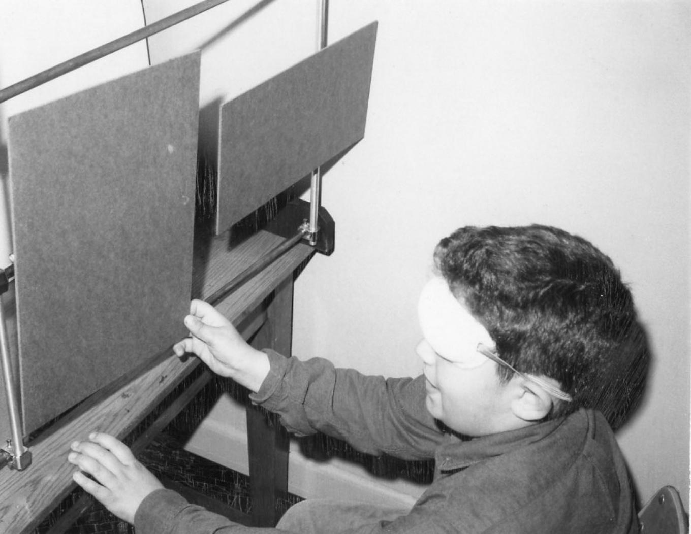 1960s era photo of a young boy blindfolded reaching for a board in a research setting