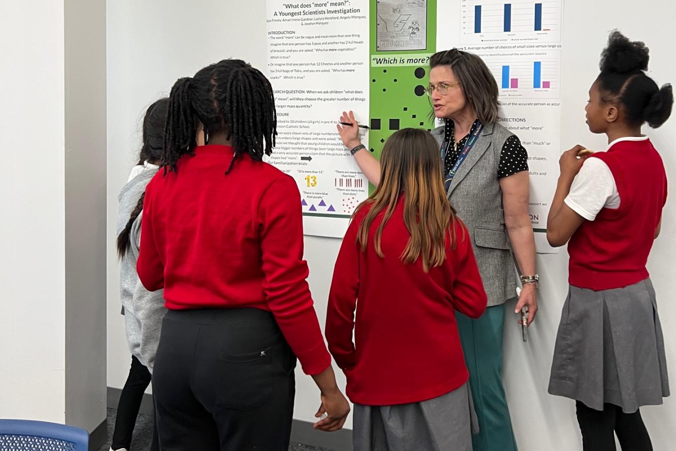 ICD Professor Melissa Koenig stands in front of a research poster with a group of middle school students