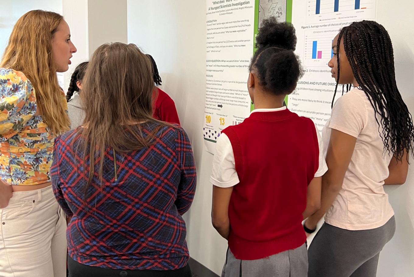 Middle school students stand in front of a research poster presenting to two graduate students
